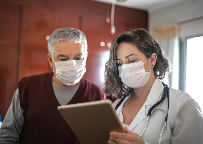 Male patient and female doctor wearing masks view a tablet together.