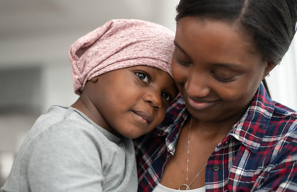 Child wearing head scarf cuddles and rests head on shoulder of a woman