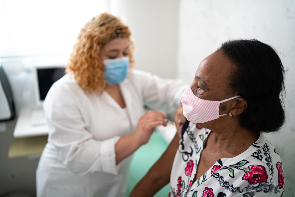A nurse administering a vaccine to an older Black woman.