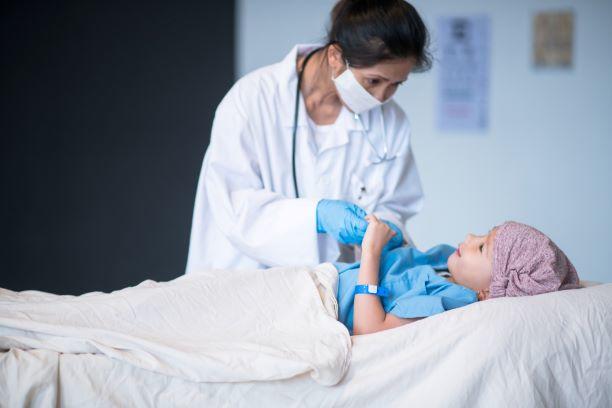 A female doctor talks with a child laying in a hospital bed.