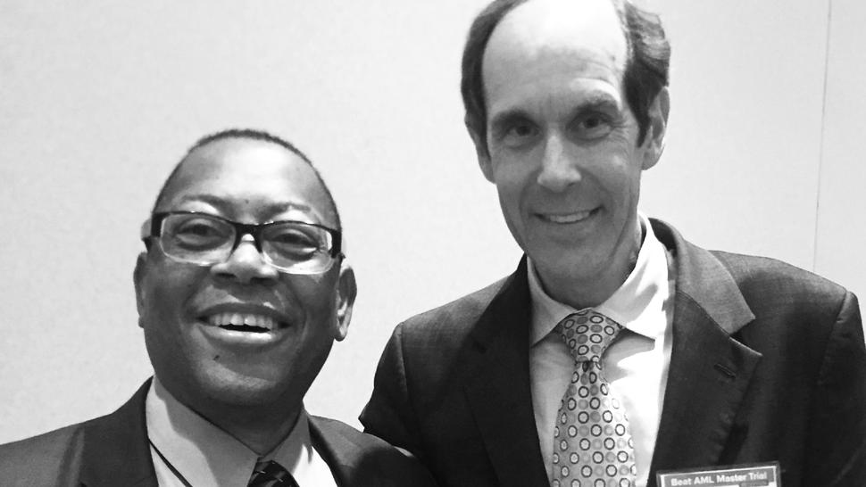 Black and white photo of two men in suits standing side-by-side and smiling at the camera. 