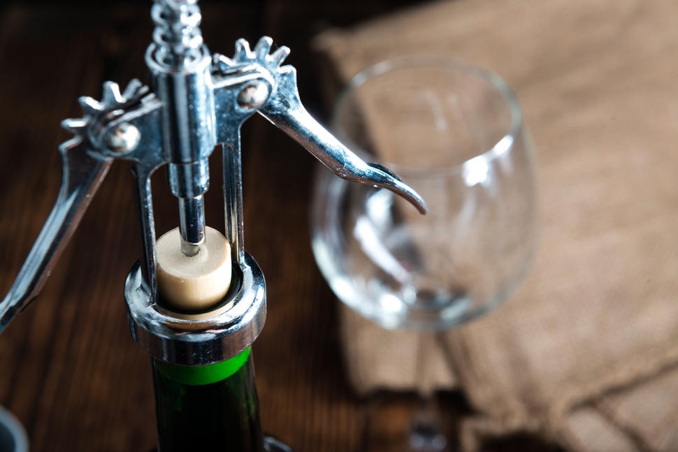 A bottle of wine being opened with a metal opener.