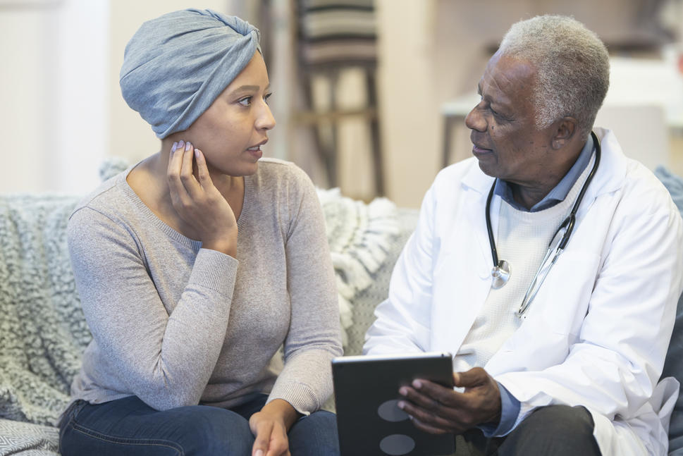 Older Black doctor speaks with younger Black woman with cancer