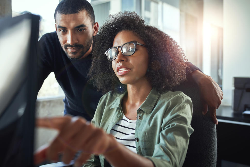 Una mujer y un hombre negro mirando la pantalla de una computadora.