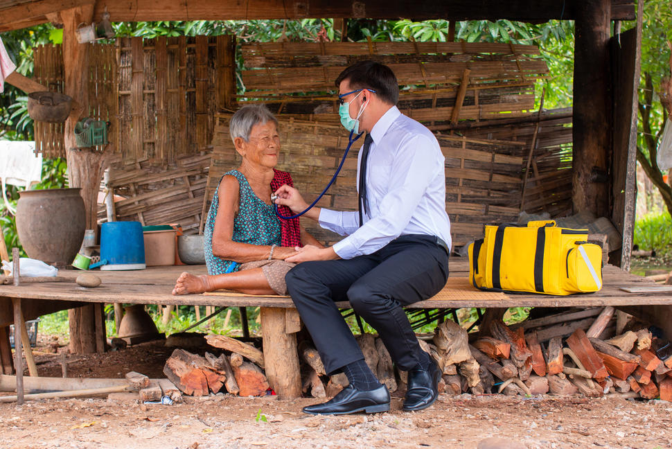 A doctor wearing a protective mask uses a stethoscope to listen to the heartbeat and breathing of an elderly woman