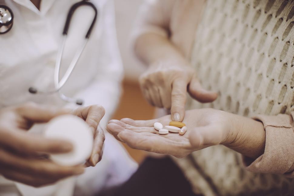 An older woman with a handful of oral medications.