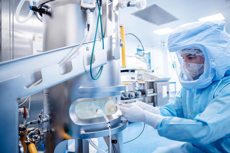 A technician in full body protective gear adjusting a machine for making mRNA vaccines.