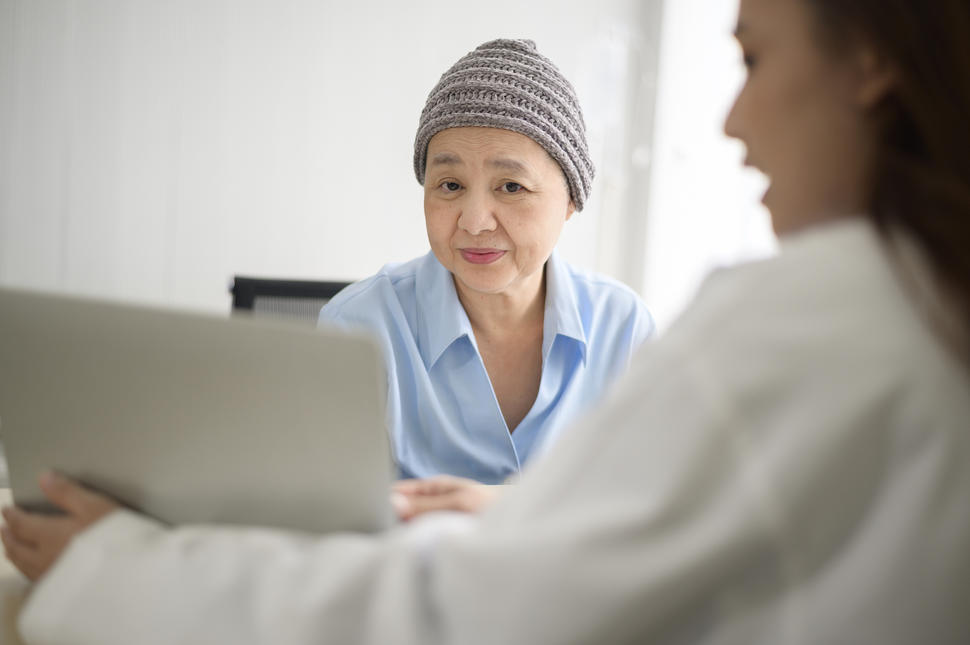 woman with scarf on her head looks at a computer screen held up by her doctor.