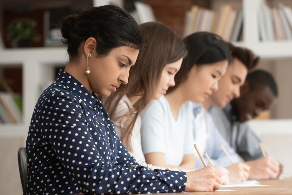 Multiracial students sitting at desk writing on papers doing task 