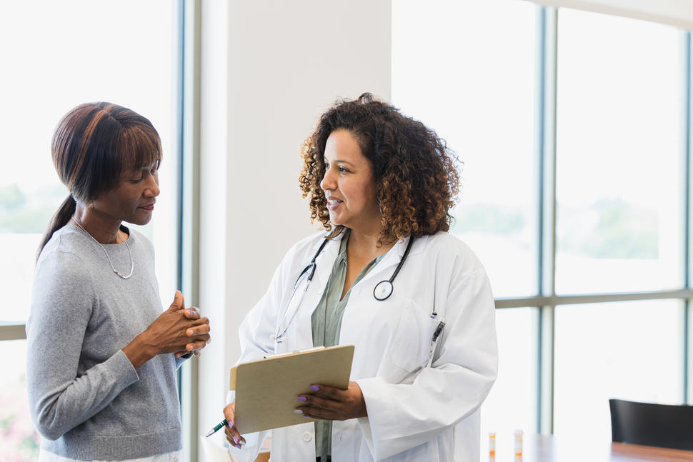 Black female patient looks at information on a tablet with female health care provider