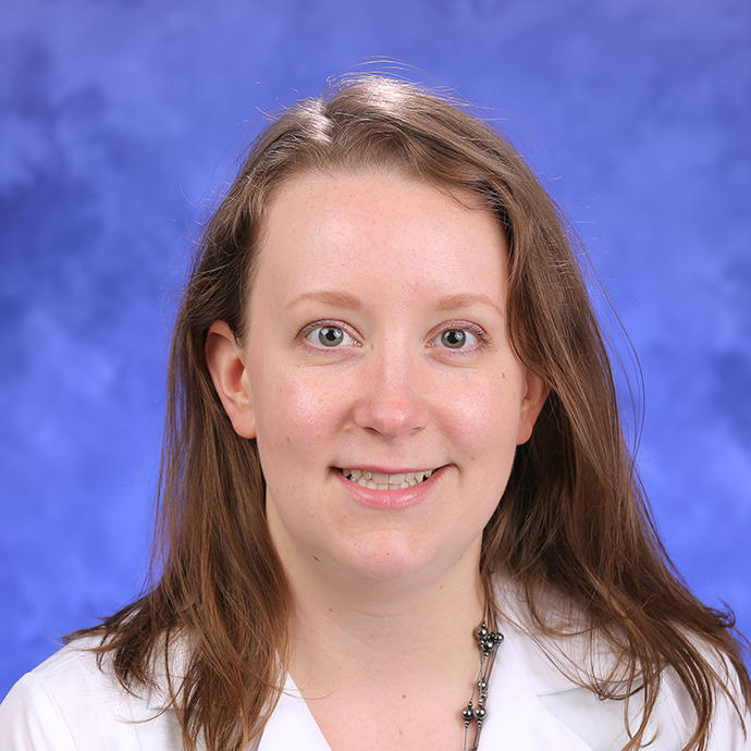 Headshot of a light-skinned woman, Jennifer Moss, in a white lab coat against a blue backdrop