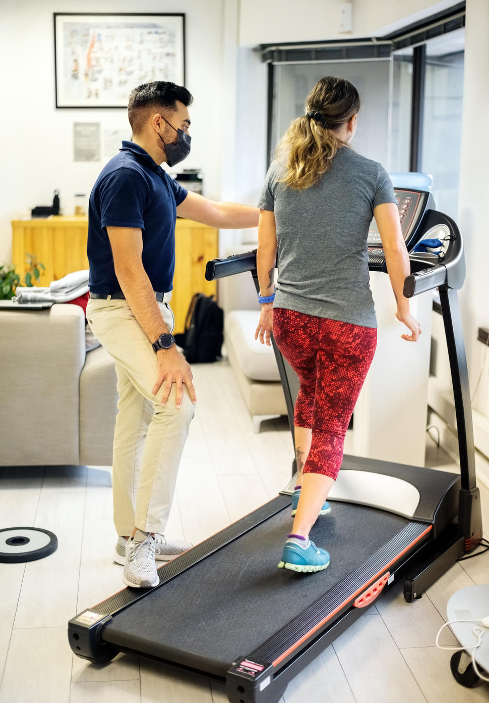A woman walking on a treadmill with a young male physical therapist supervising.