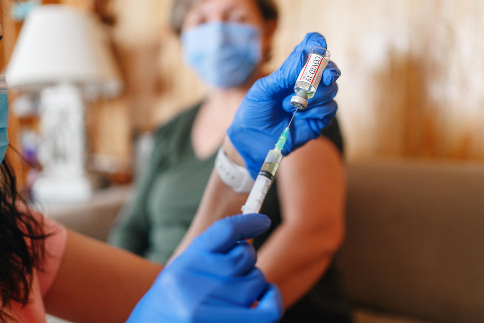 Health care provider filling syringe with COVID-19 vaccine with a senior woman in the background.