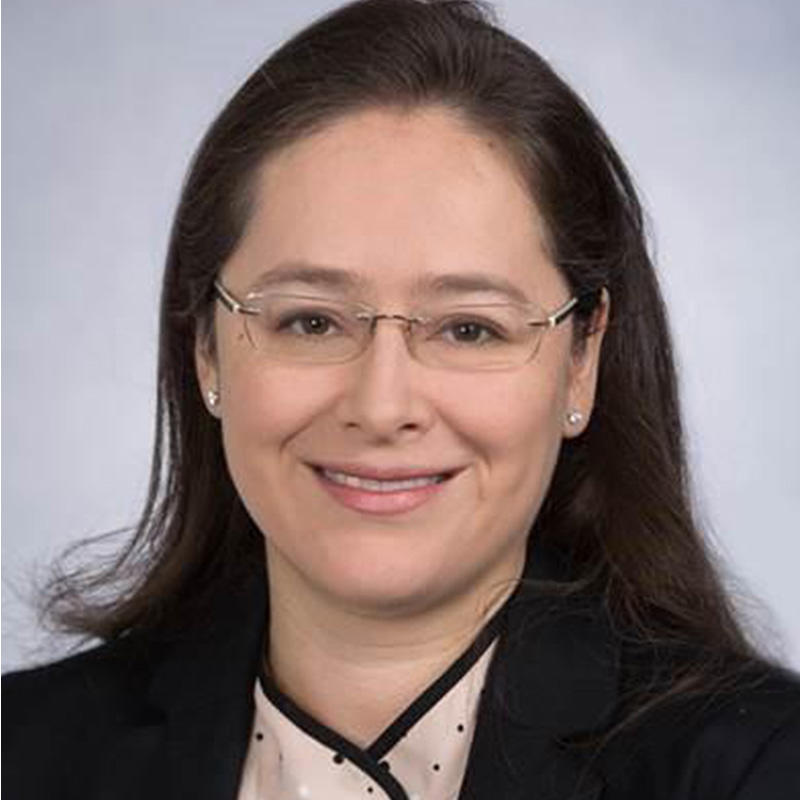 A professional headshot of Dr. Paula Aristizabal, a Latina with a light skin tone, dark hair, and glasses, smiling at the camera.