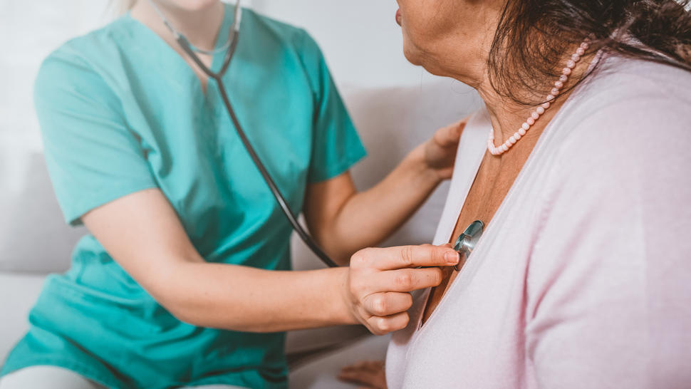 A health provider holding a stethoscope to a woman's chest.