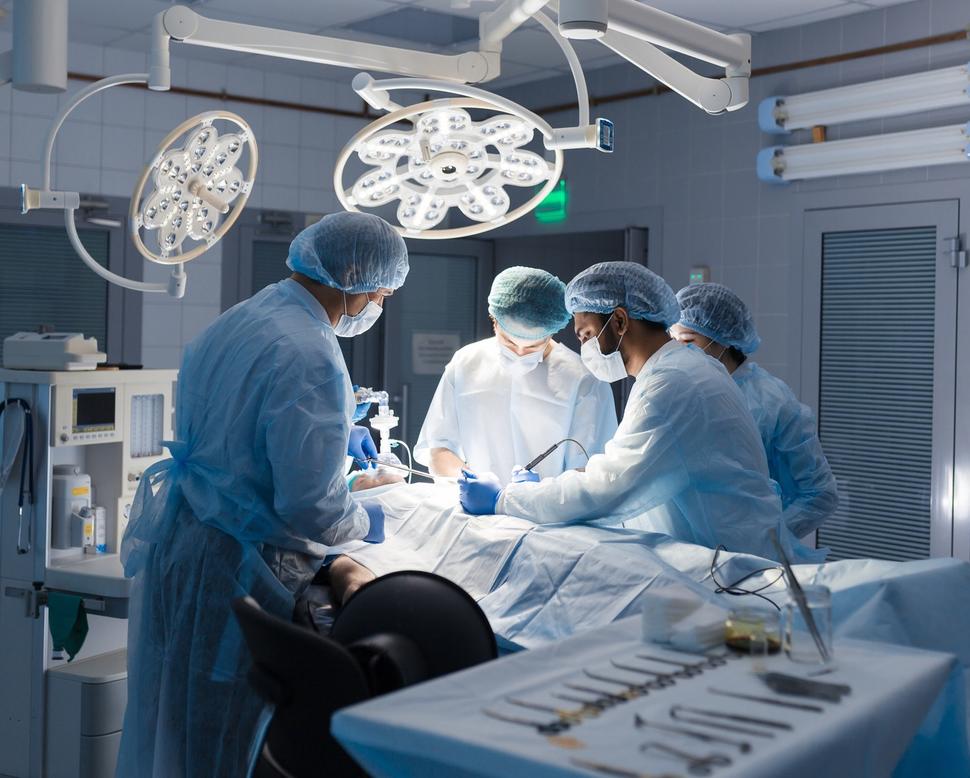 A surgical team of 2 men and 2 women standing over a patient on a table in a surgery suite.