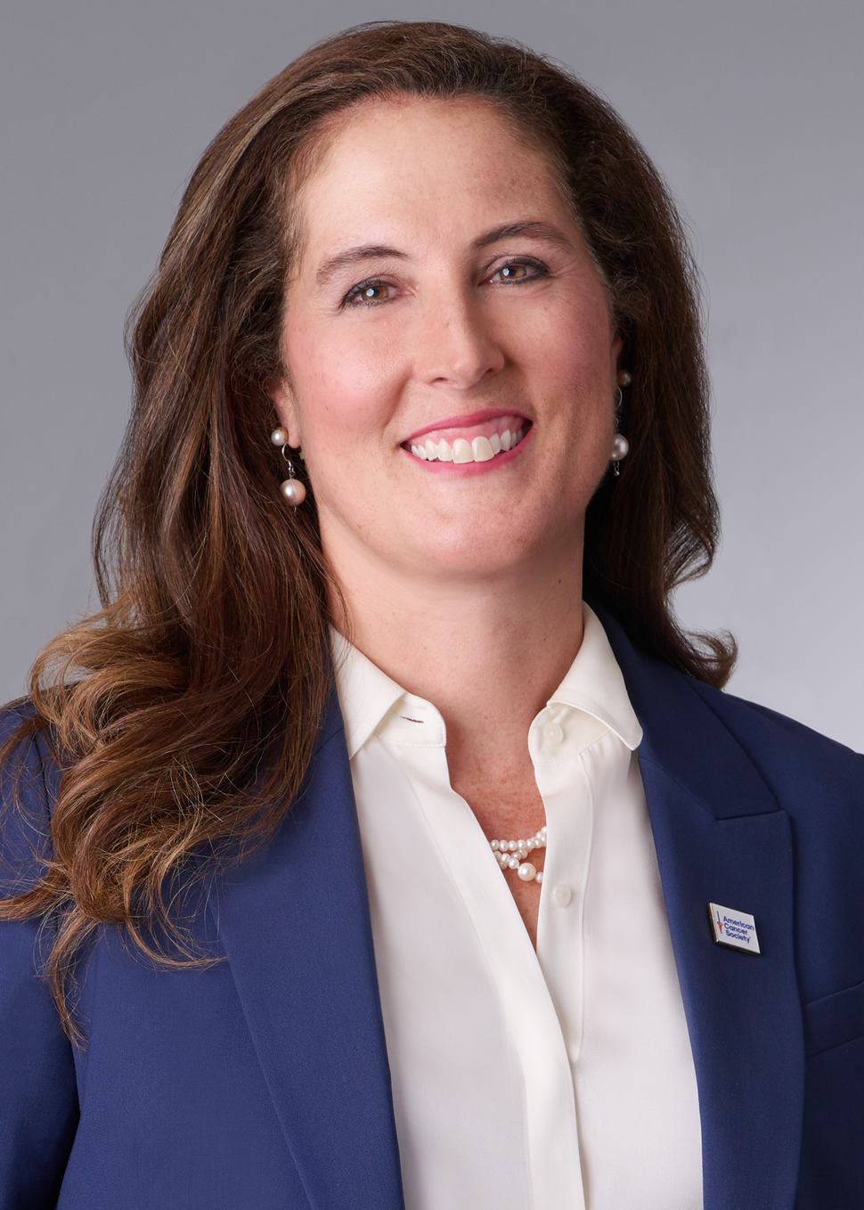 Woman with brown hair, white blouse, and blue blazer smiling