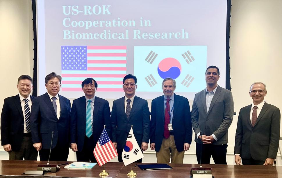 Representatives from US NCI and Republic of Korea stand in front of respective flags after signing of Memorandum of Understanding event