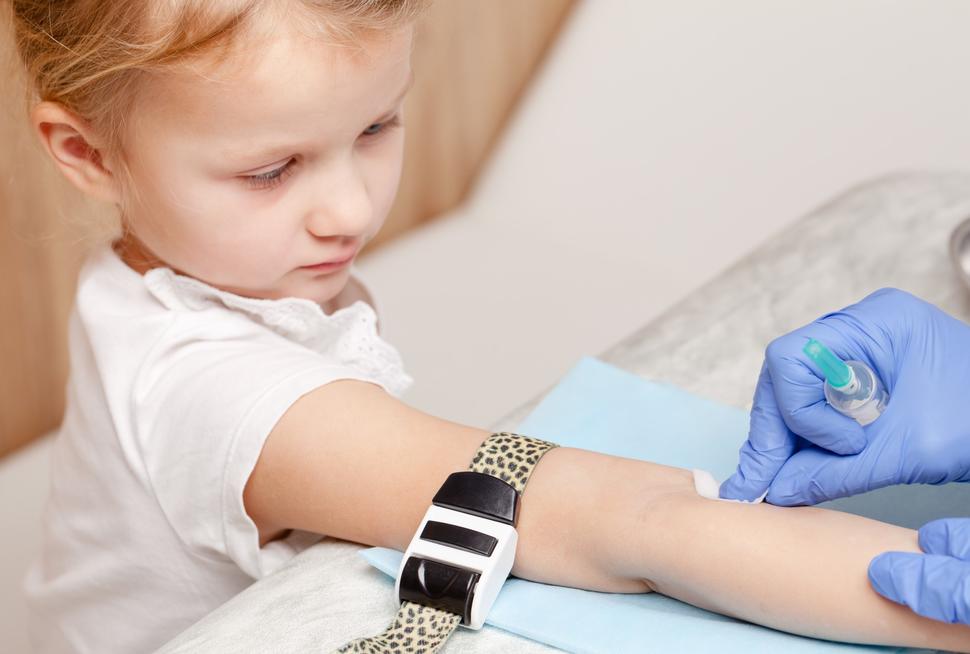 A young girl with her arm out and gloved hands cleaning a spot on her arm with a swab.