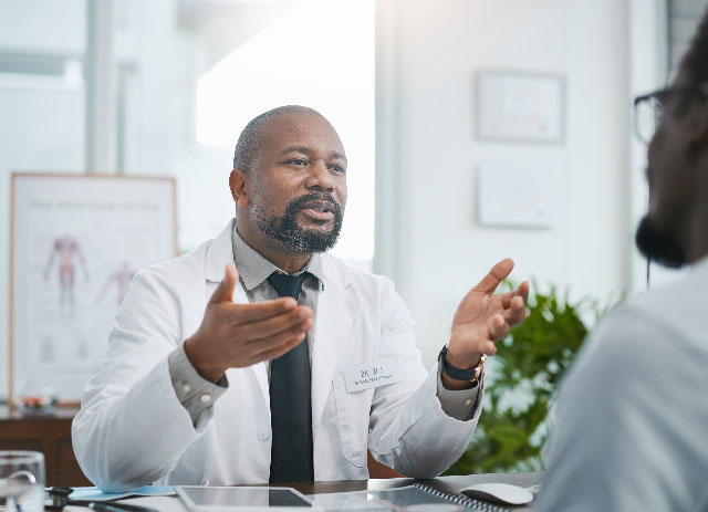 Photo of a doctor sitting at a desk speaking with a patient.