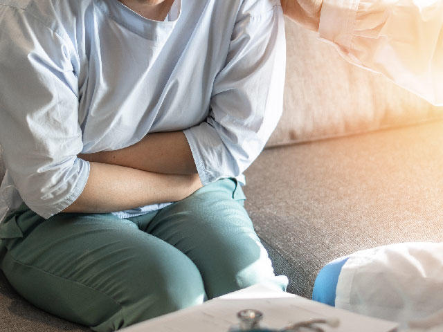 Fotografía de una mujer sentada en un sillón, inclinada un poco hacia adelante, con los brazos cruzados sobre el abdomen.