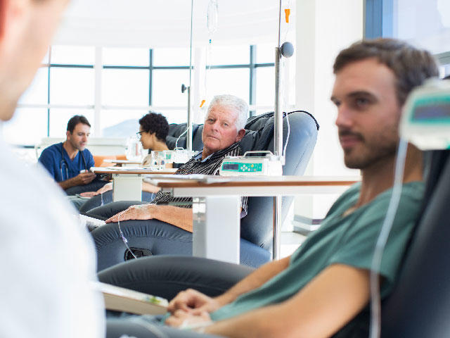 Photo of doctors talking to patients receiving intravenous (IV) medical treatment in an infusion room of a healthcare facility.