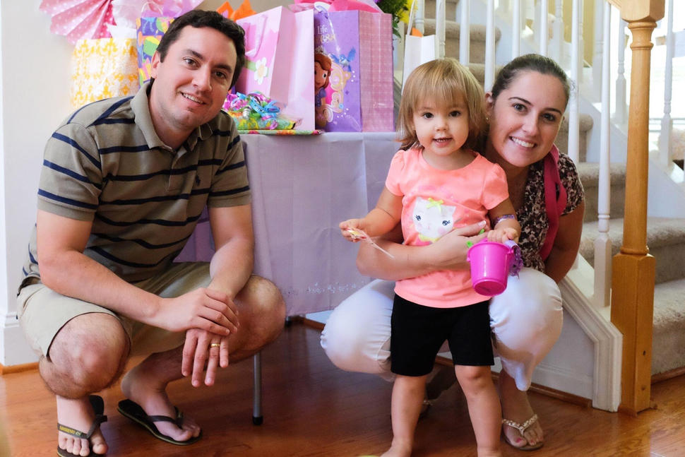 Joe and Erika smile and crouch next to their daughter, Melissa. Erika’s arm is around Melissa, who holds a small plastic bucket and smiles at the camera.