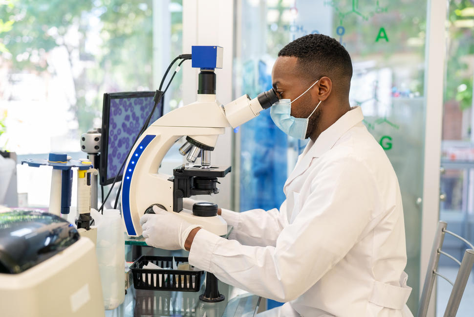 Man in a white lab coat looking into a microscope