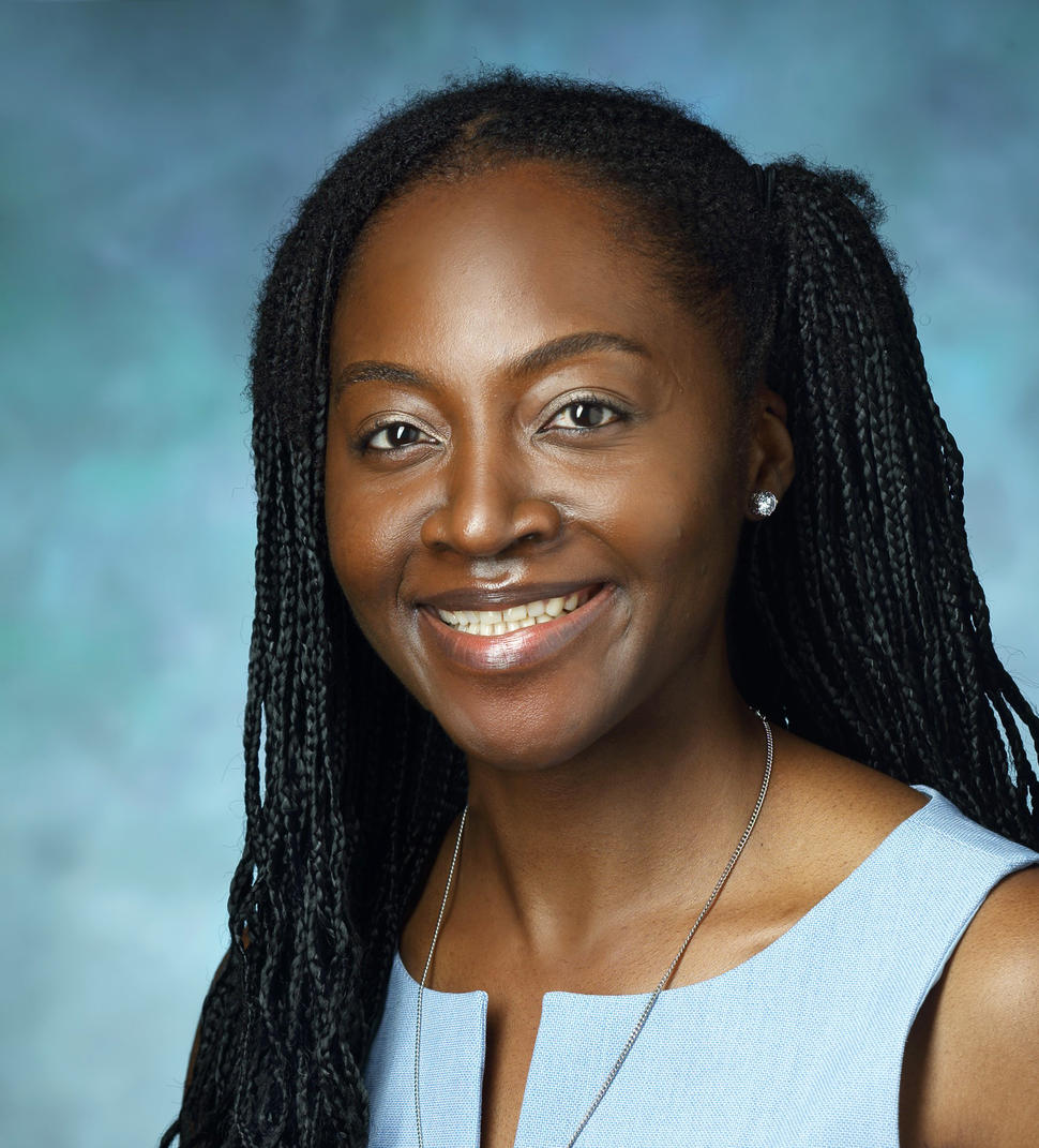 A woman, Dr. Ethel Ngen, with braided black hair and dark brown eyes wearing a light blue blouse smiles at the camera.