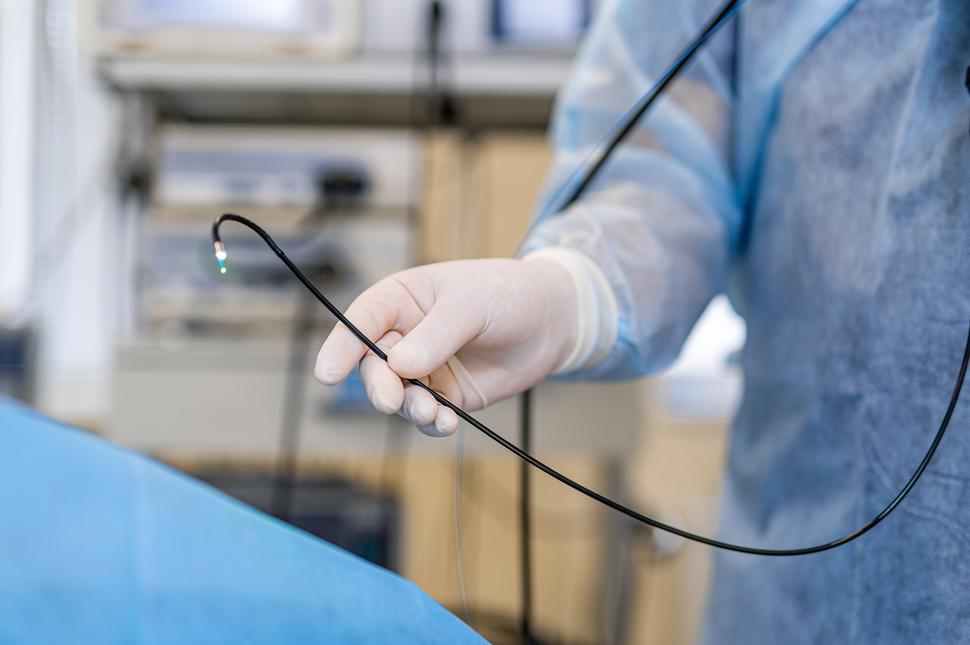 A partial image of a doctor holding a colonoscope near a patient in the endoscopy suite.