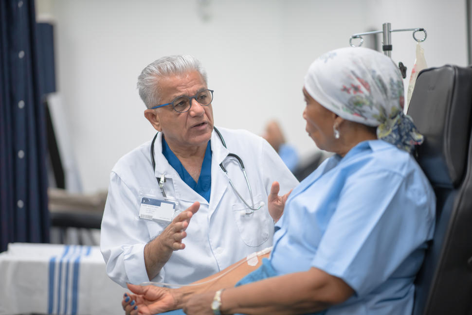 A female patient with an IV in her arm has a conversation with a male doctor. 