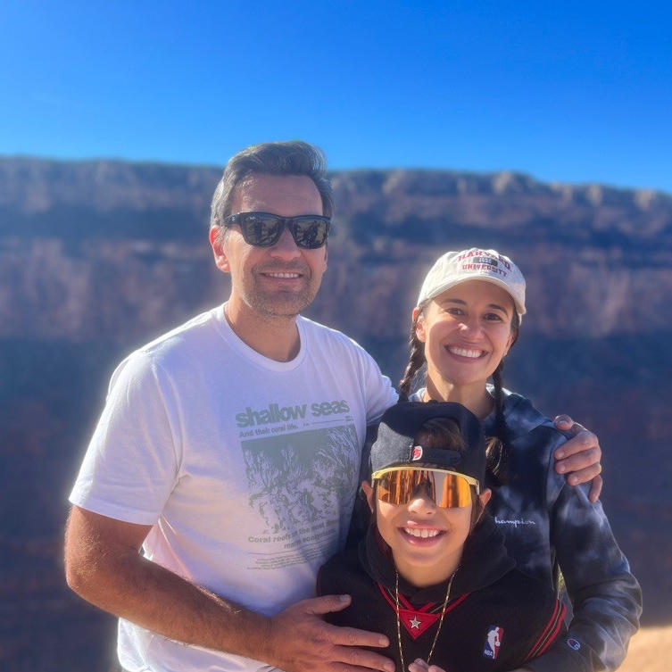 Woman, Dr. Fernanda Michels, with two long braids wearing a ballcap and sweater with her husband and young son at the Grand Canyon.