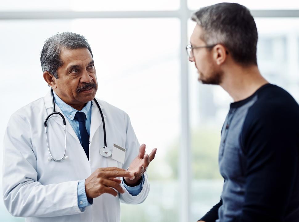 An older male doctor talking with a middle-aged male patient.