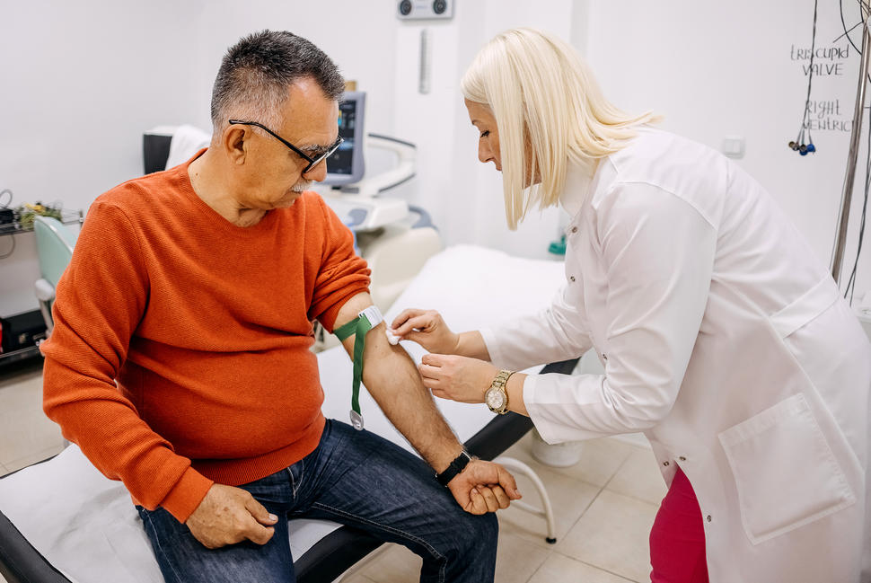 An older man gets his blood drawn by a female nurse. 