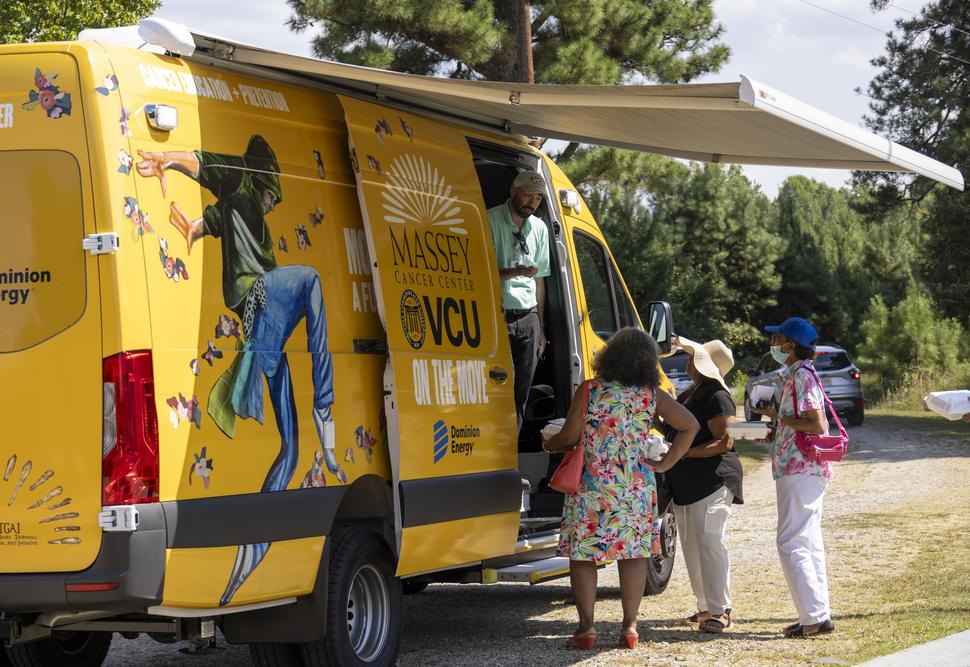 A brightly decorated van with a health care working speaking to several people from the van's side door.