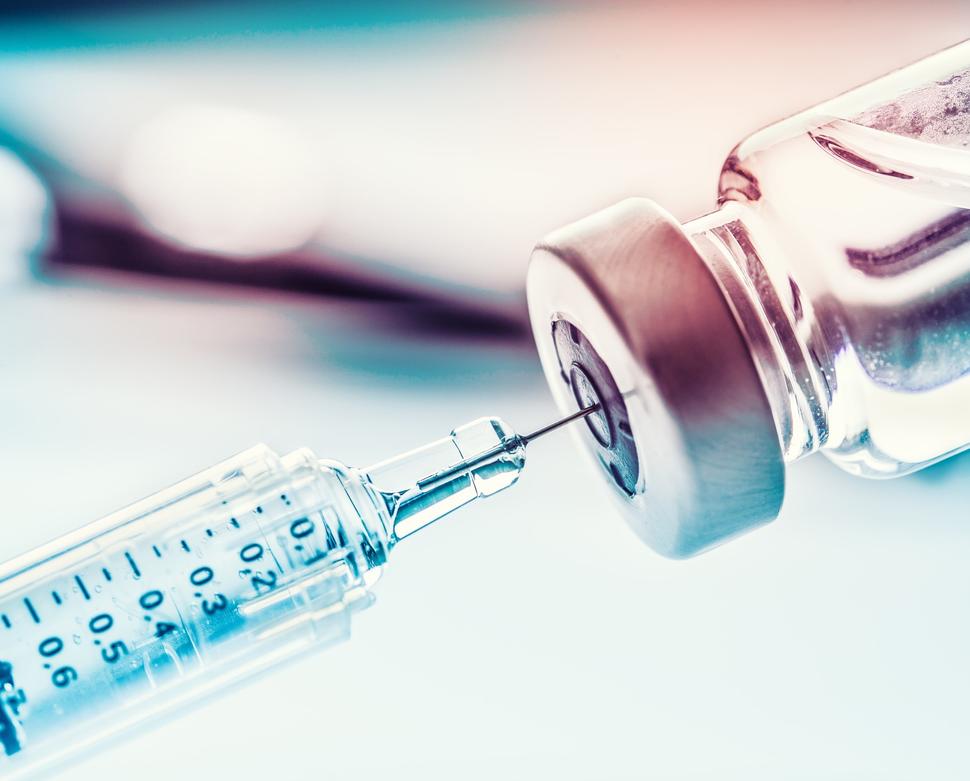 A photograph of a syringe drawing medicine from a glass vial.