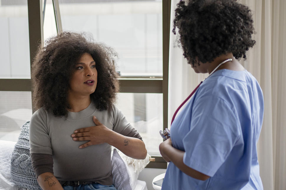 Photo of a transgender woman speaking with a health care provider wearing blue scrubs.