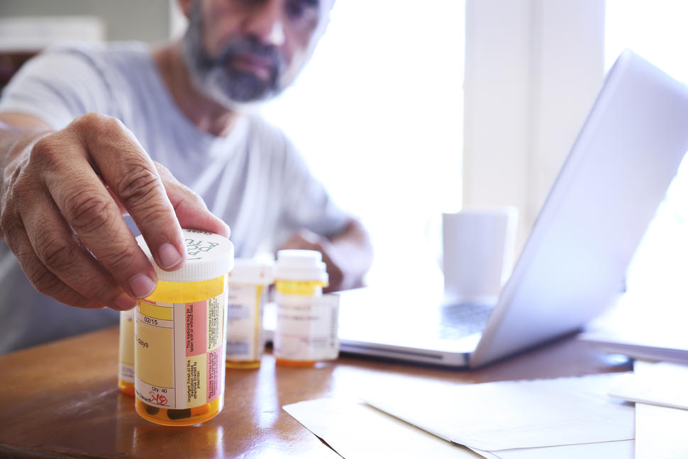 Photo of a man reaching for prescription pill bottles sitting on a table in the foreground.