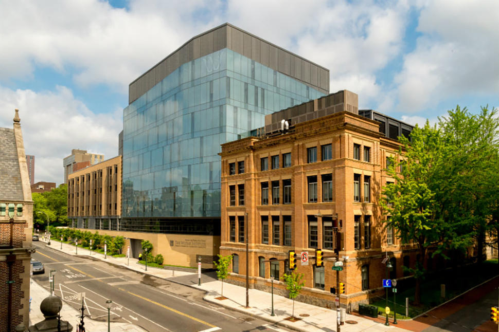 Modern architecture of The Wistar Institute featuring a striking glass cube addition connected to a historic brick building. The contemporary blue-glass structure rises several stories above the original brownstone research facility.