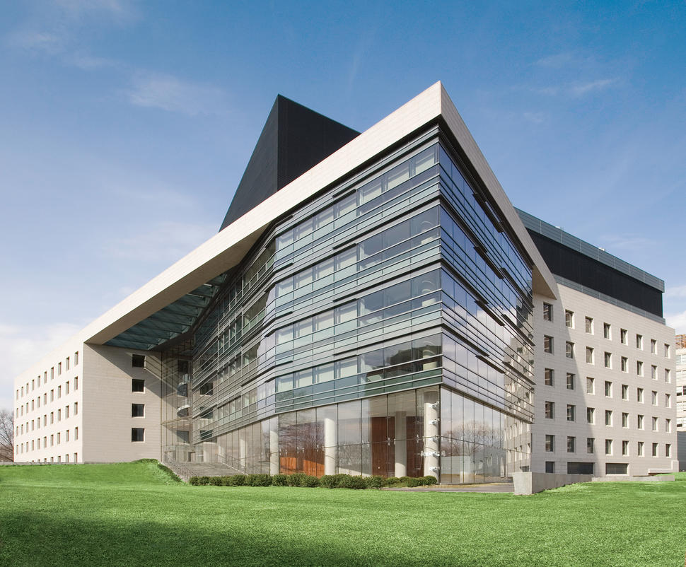 Modern glass-and-stone Albert Einstein College of Medicine building with sharp angular rooflines and a large lawn in front under a clear sky.