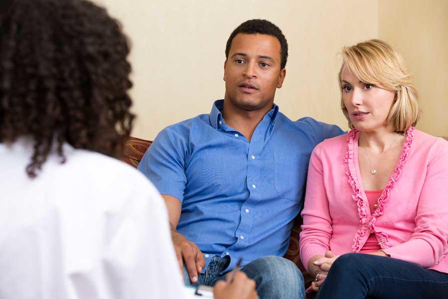 Man and woman sitting together, listening to health professional who sits across from them.