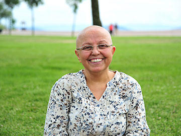 Una mujer sin cabello muy sonriente, a sus espaldas se ve un área verde