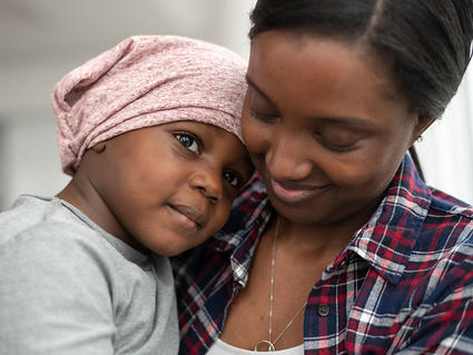 Child wearing head scarf cuddles and rests head on shoulder of a woman