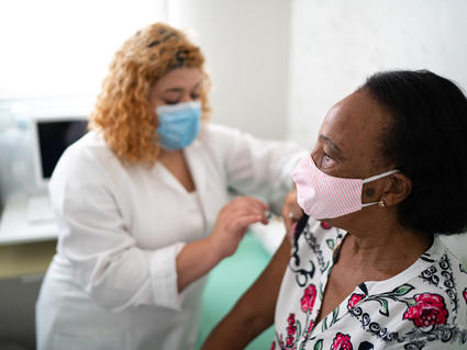 A nurse administering a vaccine to an older Black woman.