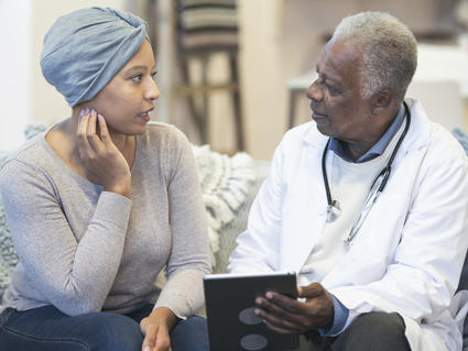 Older Black doctor speaks with younger Black woman with cancer