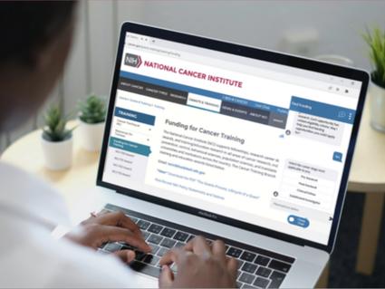 Laptop screen showing cancer.gov webpage with Find Funding Wizard/Chatbot on 