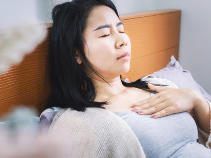 Woman laying in bed, hand on chest, in discomfort.