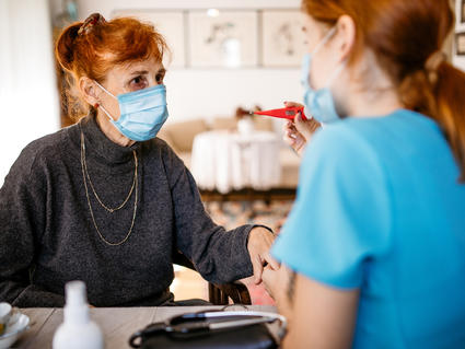 A young female community health worker taking a patient's temperature in her home.