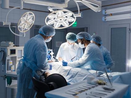 A surgical team of 2 men and 2 women standing over a patient on a table in a surgery suite.