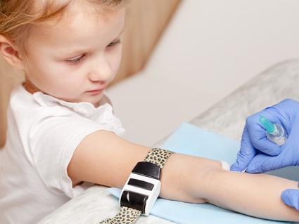 A young girl with her arm out and gloved hands cleaning a spot on her arm with a swab.